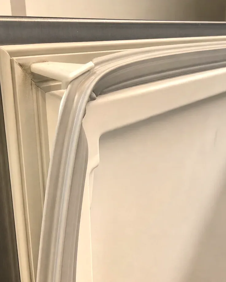 Corner of a white door gasket seated in its channel on a refrigerator door.