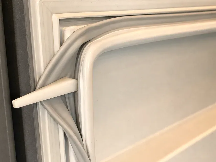 Plastic wedge lifting the edge of a white door gasket away from the door liner.