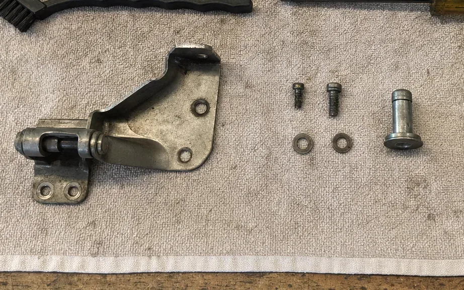 Refrigerator door hinge bracket on a towel with its screws, washers and hinge pin laid out beside it.